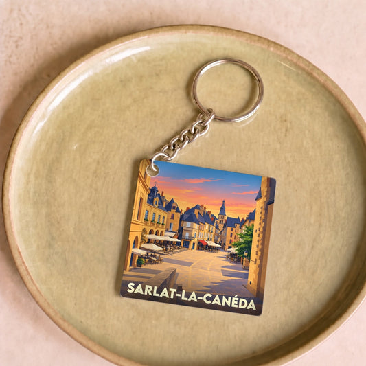 Porte-clés souvenir de Sarlat-la-Canéda illustrant une place de la ville au coucher du soleil.
