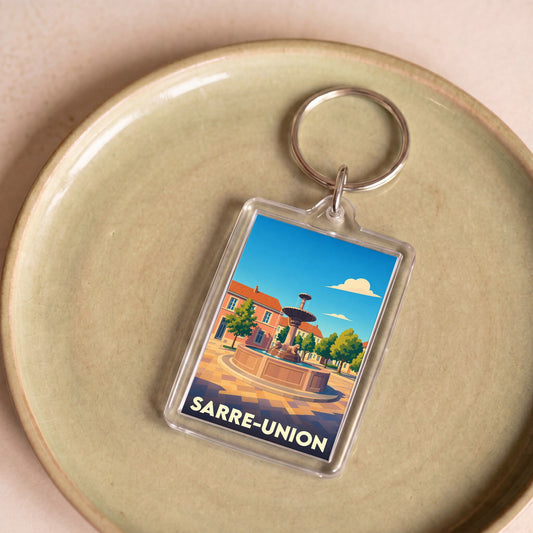 Porte-clés souvenir de la ville de Sarre-Union avec une illustration stylisée de sa place et sa fontaine.