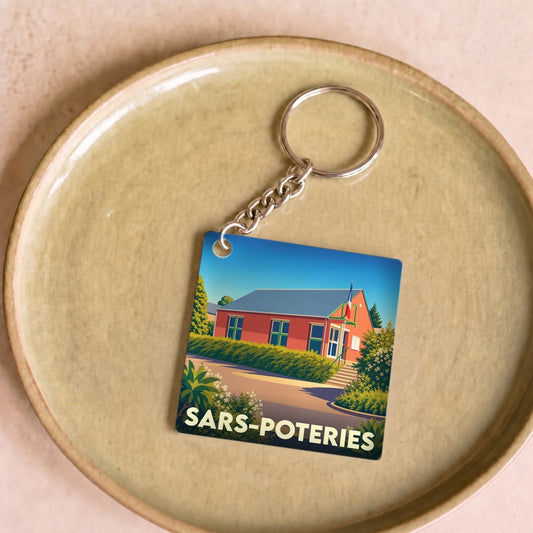 Porte-clés souvenir de la ville de Sars-Poteries avec une illustration stylisée d'un bâtiment local.