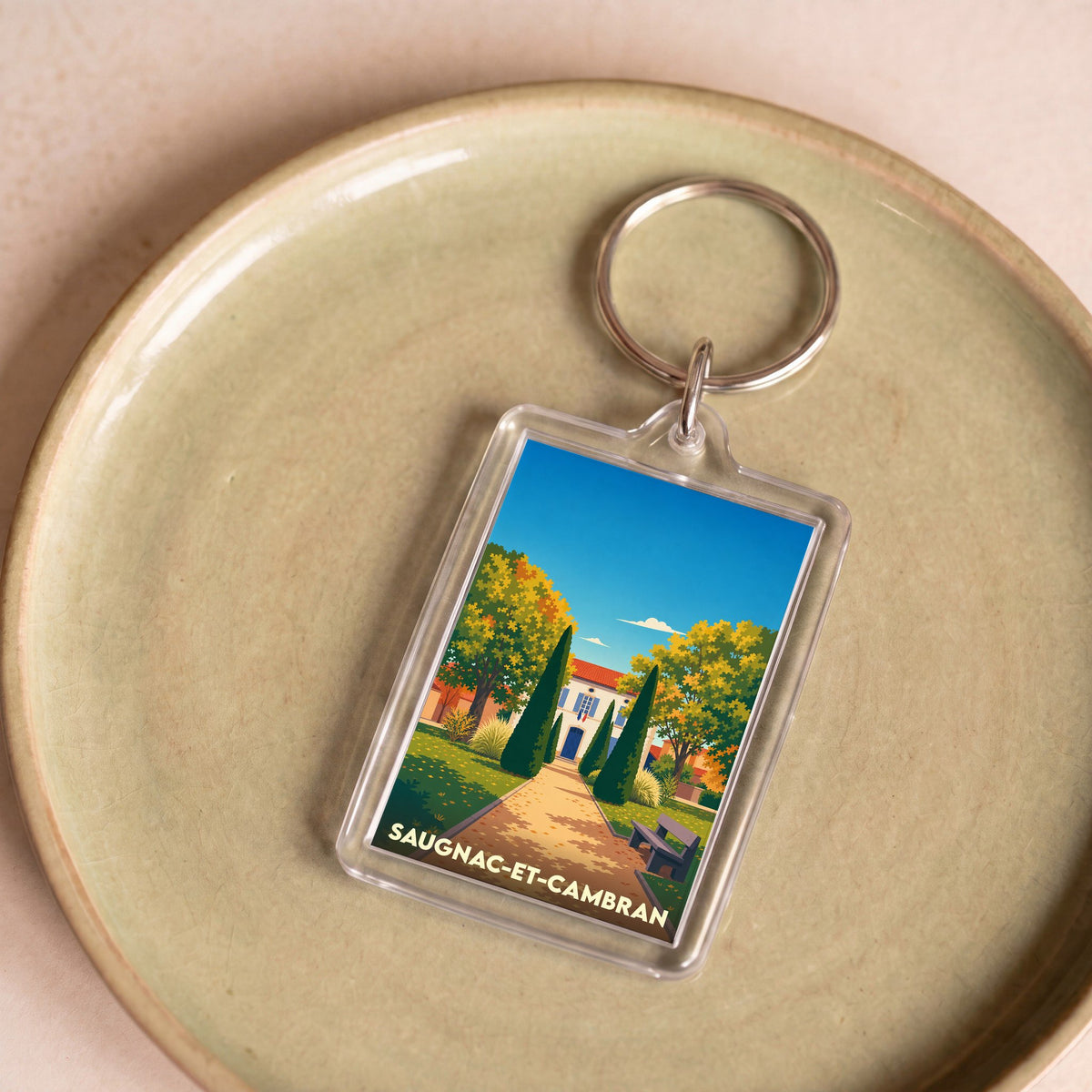 Porte-clés souvenir de la ville de Saugnac-et-Cambran avec une illustration stylisée d'un paysage ensoleillé.