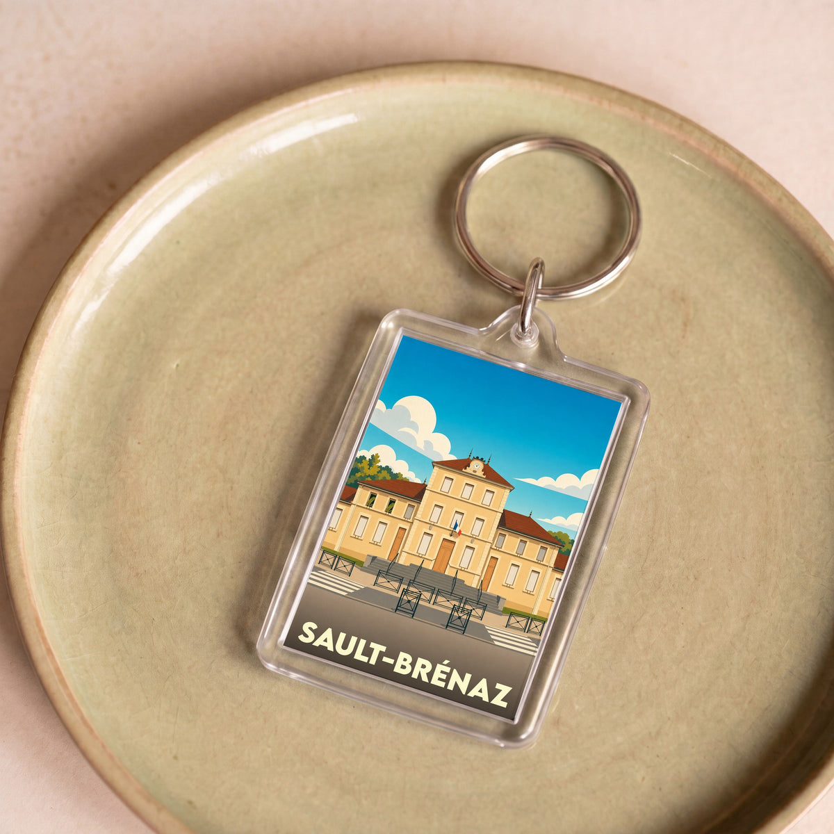 Porte-clés souvenir de la ville de Sault-Brénaz avec une illustration stylisée de sa mairie.