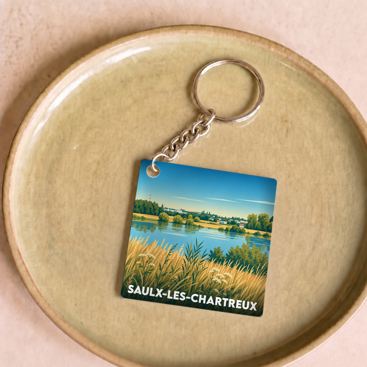 Porte-clés souvenir de la ville de Saulx-les-Chartreux avec une illustration stylisée de paysage naturel.