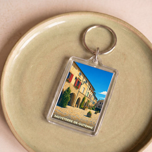 Porte-clés souvenir de la ville de Sauveterre-de-Guyenne avec une illustration stylisée d'une place historique.