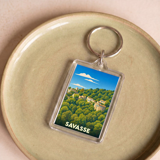 Porte-clés souvenir de la ville de Savasse avec une illustration stylisée d'un village niché dans la forêt.