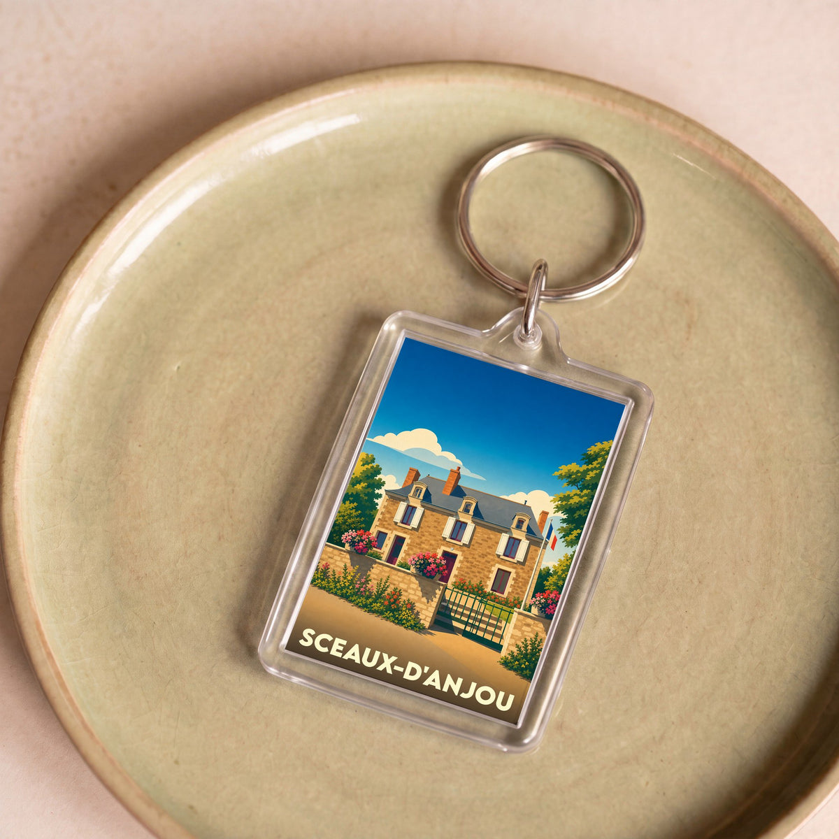 Porte-clés souvenir de la ville de Sceaux-d'Anjou avec une illustration stylisée d'une maison angevine.