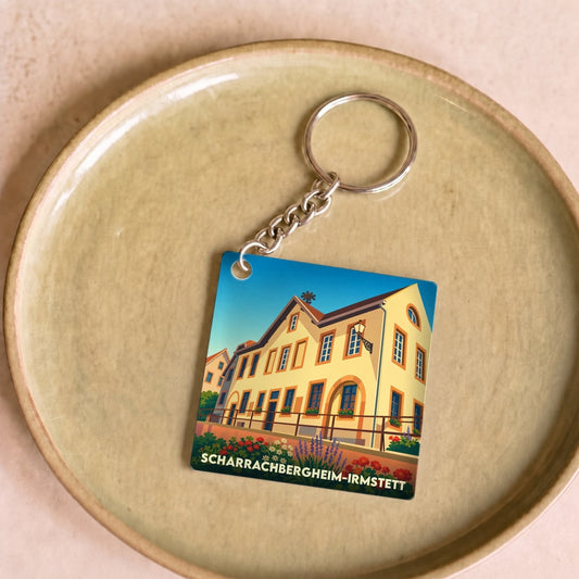 Porte-clés souvenir de la commune de Scharrachbergheim-Irmstett avec une illustration stylisée d'un bâtiment traditionnel.
