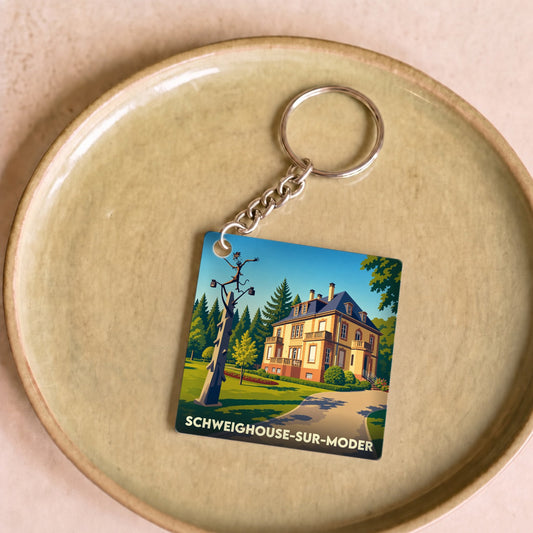 Porte-clés souvenir de Schweighouse-sur-Moder illustrant une grande demeure et un mât décoratif.