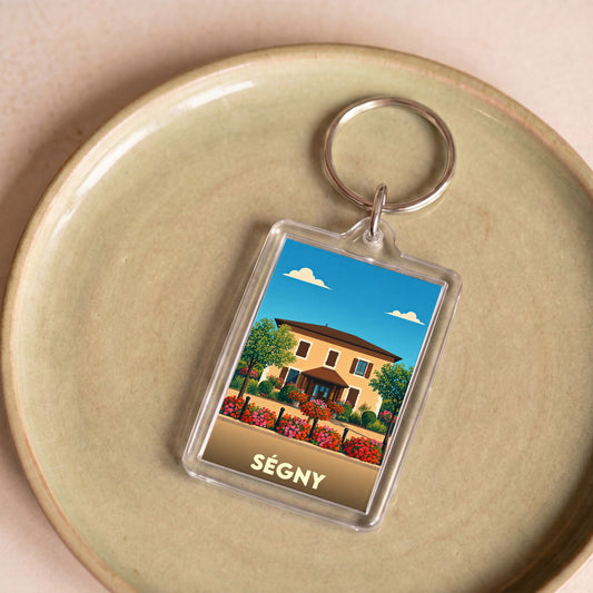 Porte-clés souvenir de la ville de Ségny avec une illustration stylisée d'une maison fleurie.