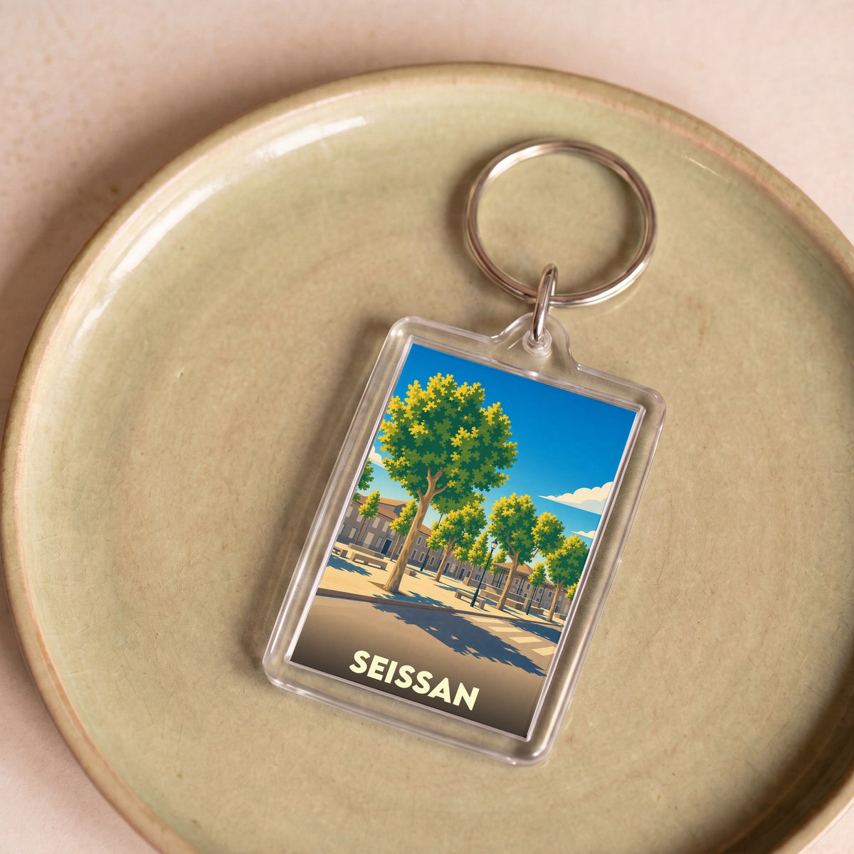 Porte-clés souvenir de la ville de Seissan avec une illustration stylisée d'une place arborée.