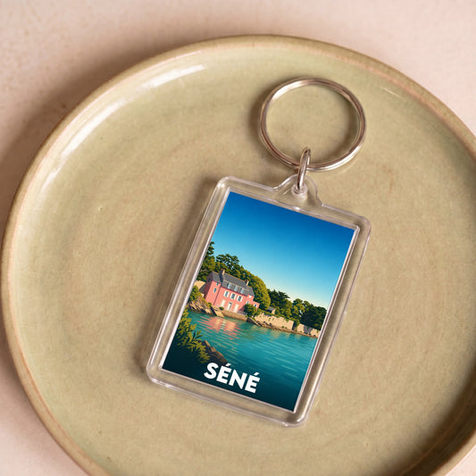 Porte-clés souvenir de la ville de Séné avec une illustration stylisée d'une maison rose en bord de mer.