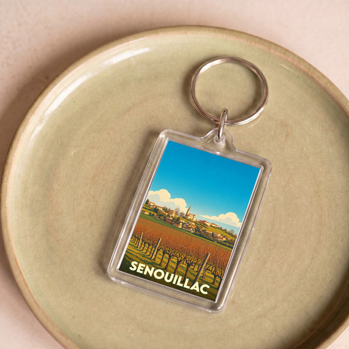 Porte-clés souvenir de la ville de Senouillac avec une illustration stylisée de ses vignobles.