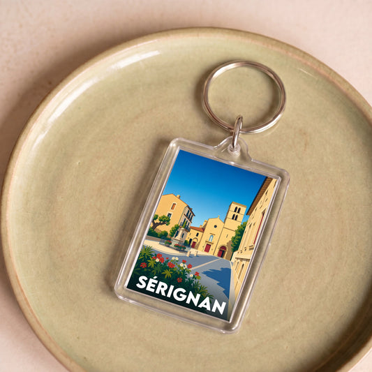 Porte-clés souvenir de la ville de Sérignan avec une illustration stylisée d'une place ensoleillée.