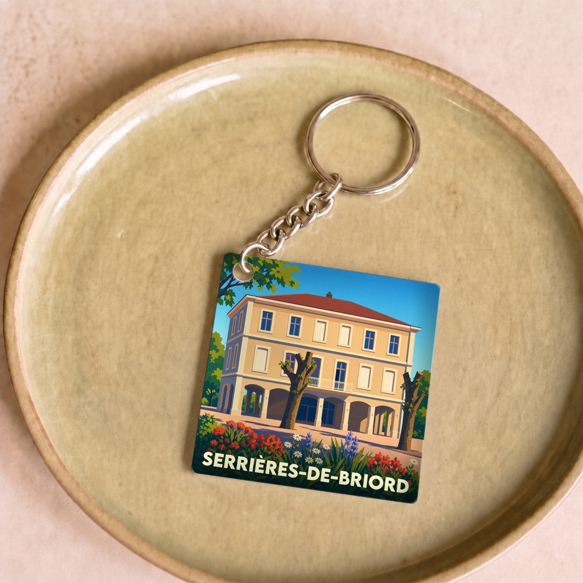 Porte-clés souvenir de la ville de Serrières-de-Briord avec une illustration stylisée d'un bâtiment fleuri.