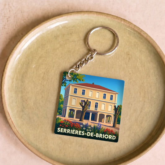 Porte-clés souvenir de la ville de Serrières-de-Briord avec une illustration stylisée d'un bâtiment fleuri.