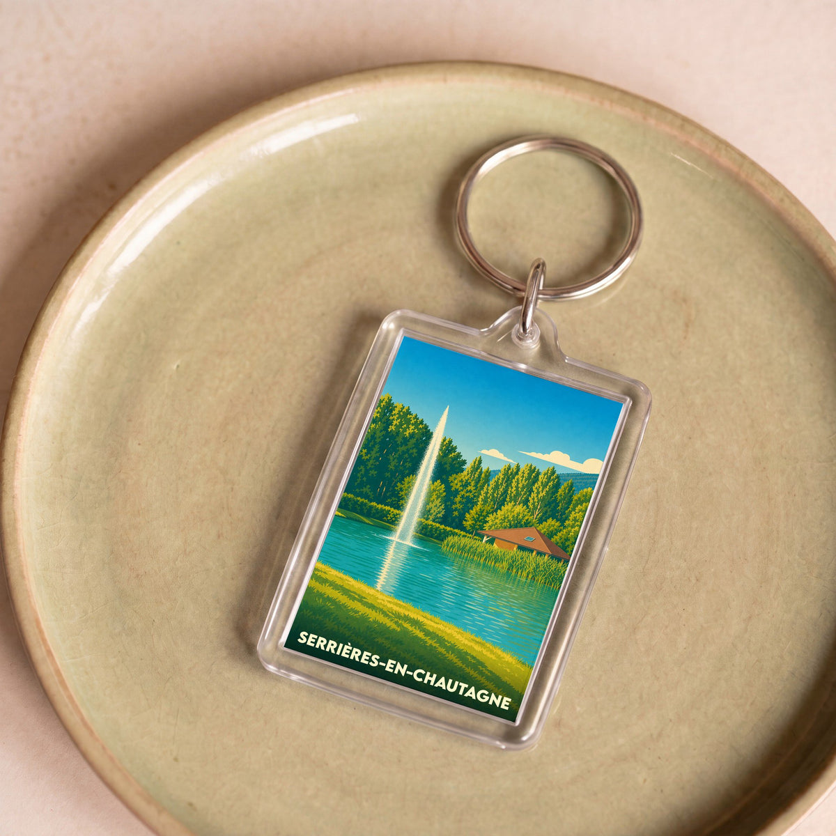 Porte-clés souvenir de Serrières-en-Chautagne avec une illustration stylisée d'un plan d'eau et de son jet d'eau.