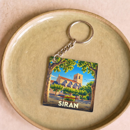 Porte-clés souvenir de la ville de Siran avec une illustration stylisée de son église et de sa place arborée.