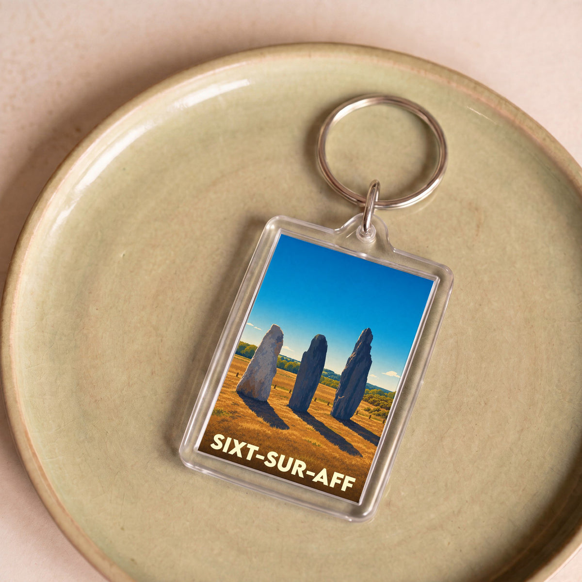 Porte-clés souvenir de la ville de Sixt-sur-Aff avec une illustration stylisée de menhirs.
