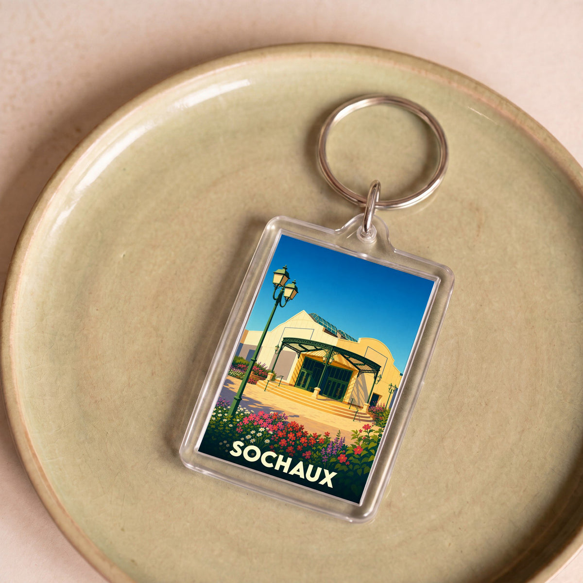 Porte-clés souvenir de la ville de Sochaux avec une illustration stylisée d'un bâtiment emblématique.