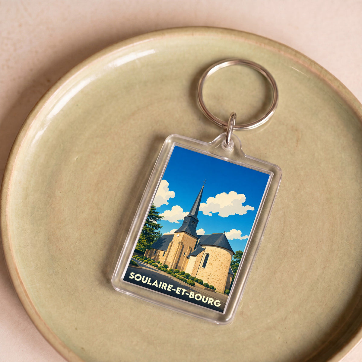 Porte-clés souvenir de la ville de Soulaire-et-Bourg avec une illustration stylisée de son église.