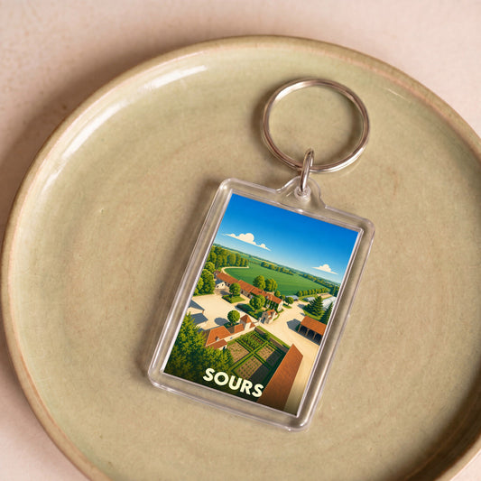 Porte-clés souvenir de la ville de Sours avec une illustration stylisée de ses paysages ruraux.