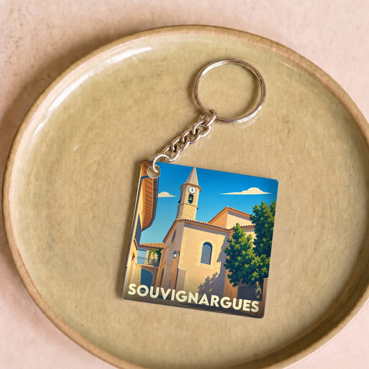 Porte-clés souvenir de la ville de Souvignargues avec une illustration stylisée de son église sous un ciel bleu.