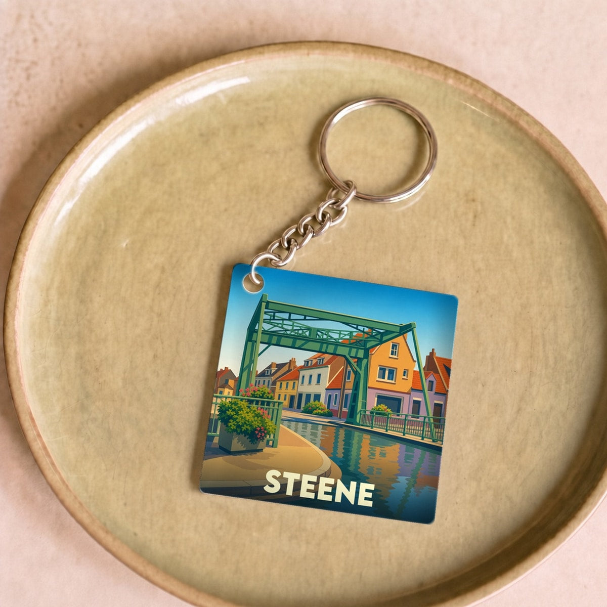Porte-clés souvenir de la ville de Steene avec une illustration stylisée de son pont et du canal.