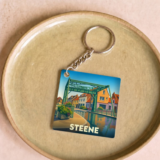 Porte-clés souvenir de la ville de Steene avec une illustration stylisée de son pont et du canal.