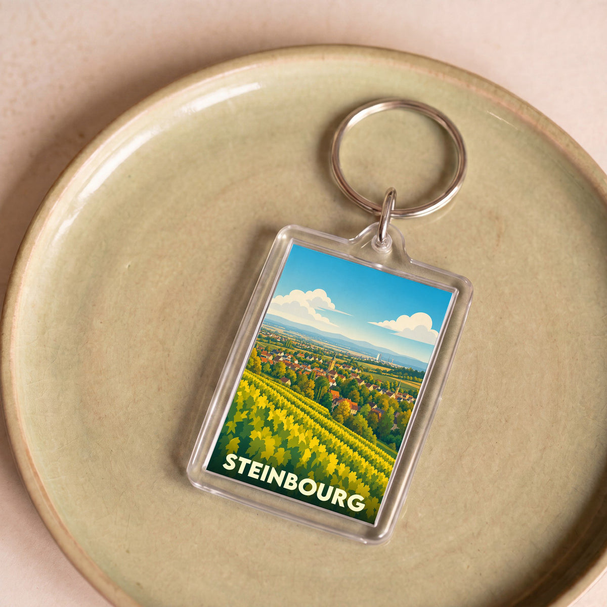 Porte-clés souvenir de la ville de Steinbourg avec une illustration stylisée de son paysage de vignobles.