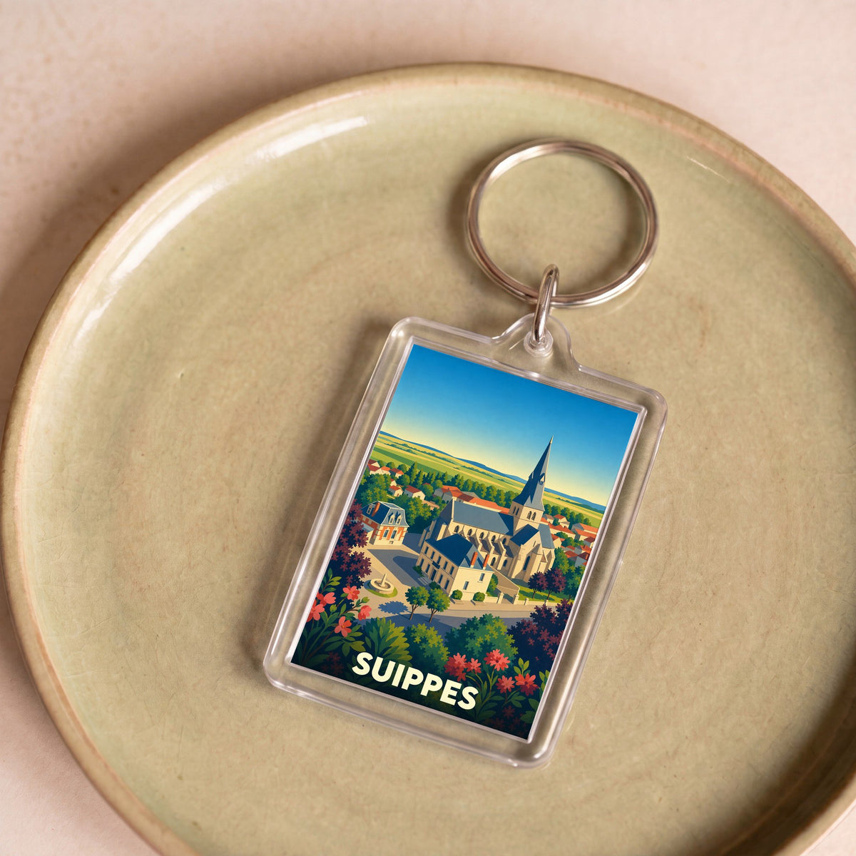 Porte-clés souvenir de la ville de Suippes avec une illustration stylisée d'une église et de paysages ruraux.
