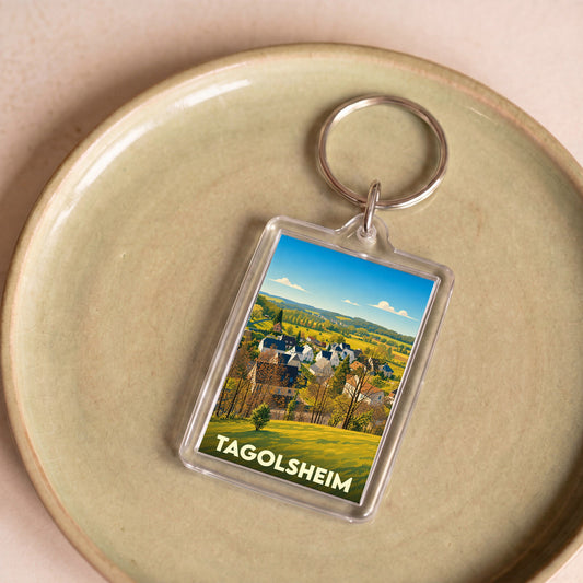 Porte-clés souvenir de la ville de Tagolsheim avec une illustration stylisée d'un paysage rural.