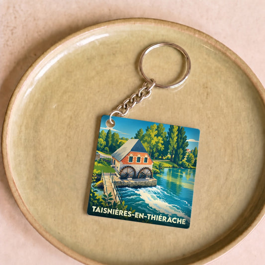 Porte-clés souvenir de la ville de Taisnières-en-Thiérache illustrant un moulin à eau au bord d'une rivière.