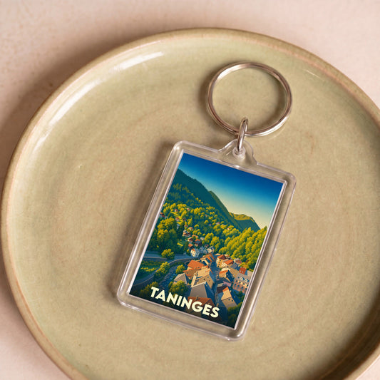 Porte-clés souvenir de la ville de Taninges avec une illustration stylisée de montagne.