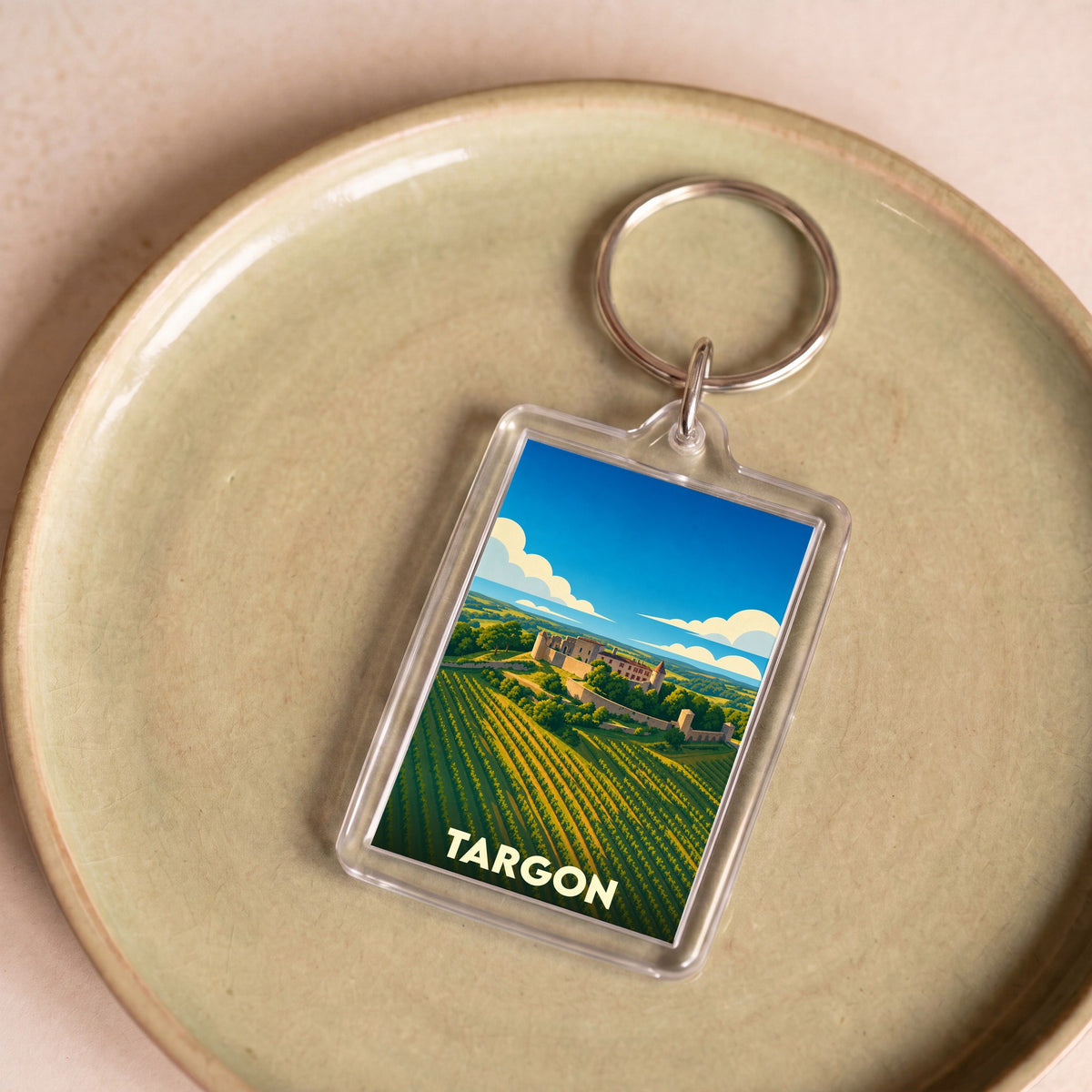 Porte-clés souvenir de la ville de Targon avec une illustration stylisée d'un paysage de vignobles et de château.