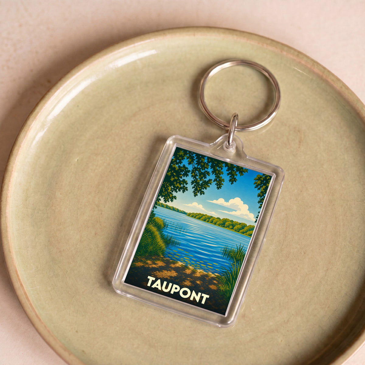 Porte-clés souvenir de la ville de Taupont avec une illustration stylisée d'un lac bordé de végétation.