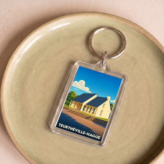 Porte-clés souvenir de la ville de Teurthéville-Hague avec une illustration stylisée d'une maison côtière.