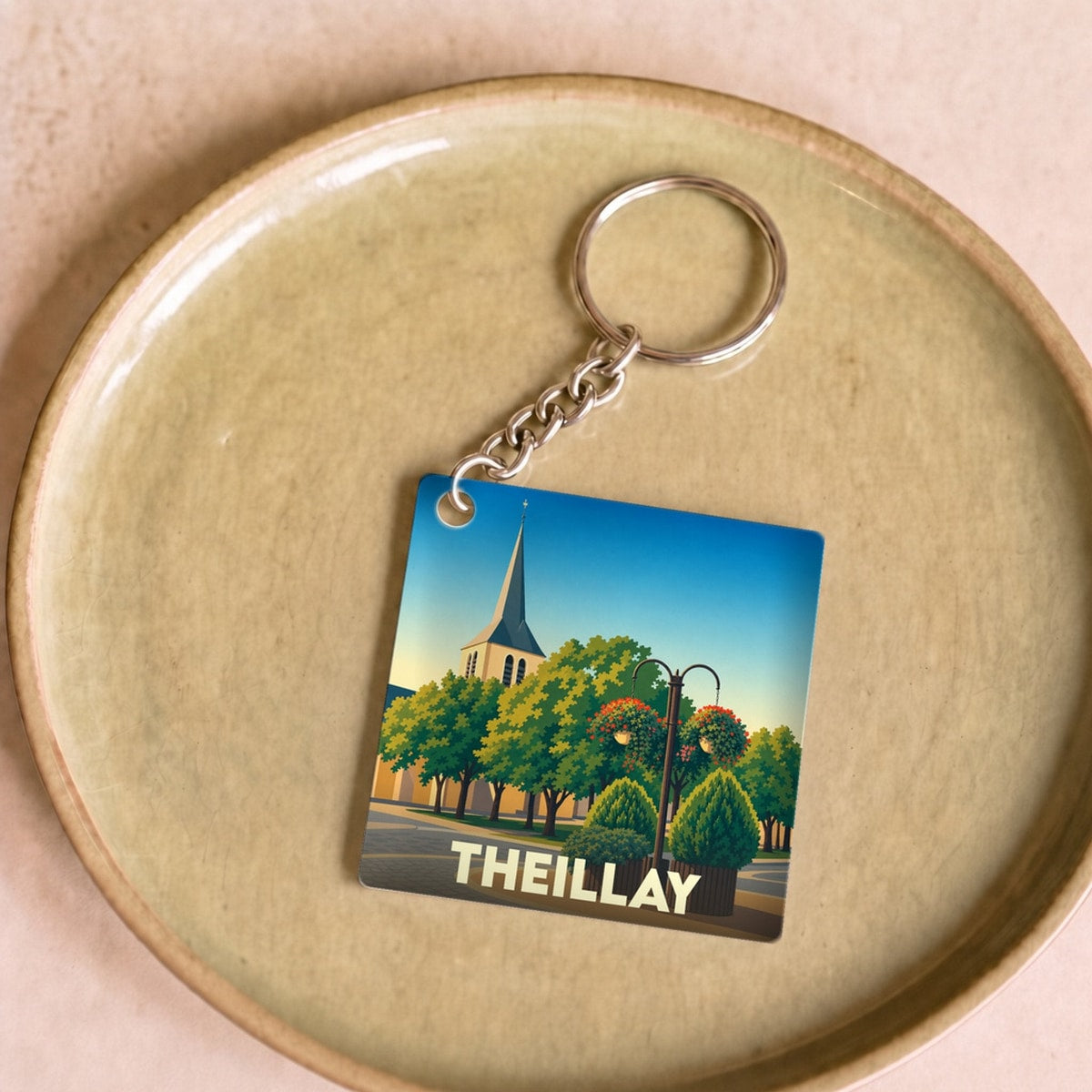 Porte-clés souvenir de la ville de Theillay avec une illustration stylisée d'un clocher et de jardins.