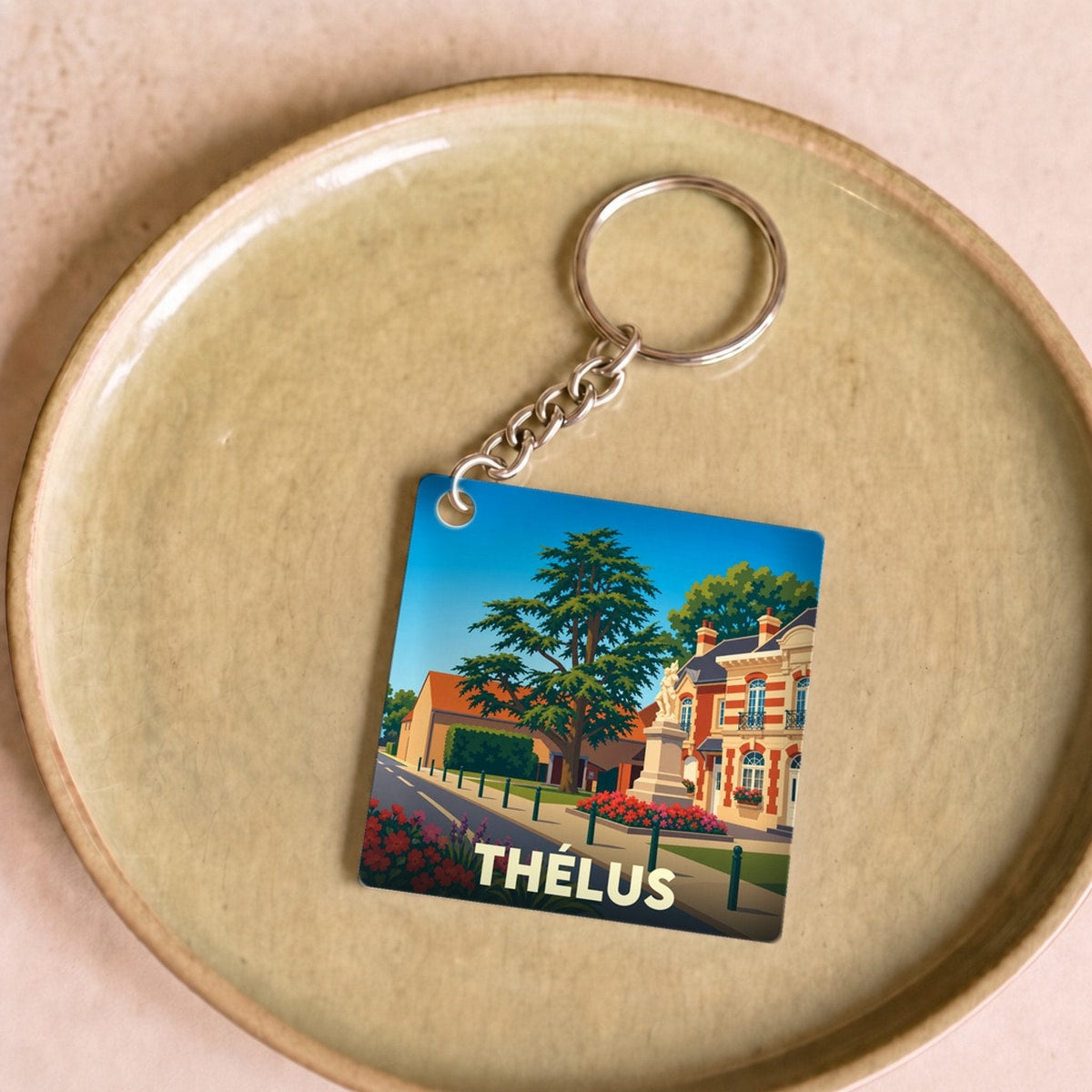 Porte-clés souvenir de la ville de Thélus avec une illustration stylisée d'un paysage urbain.