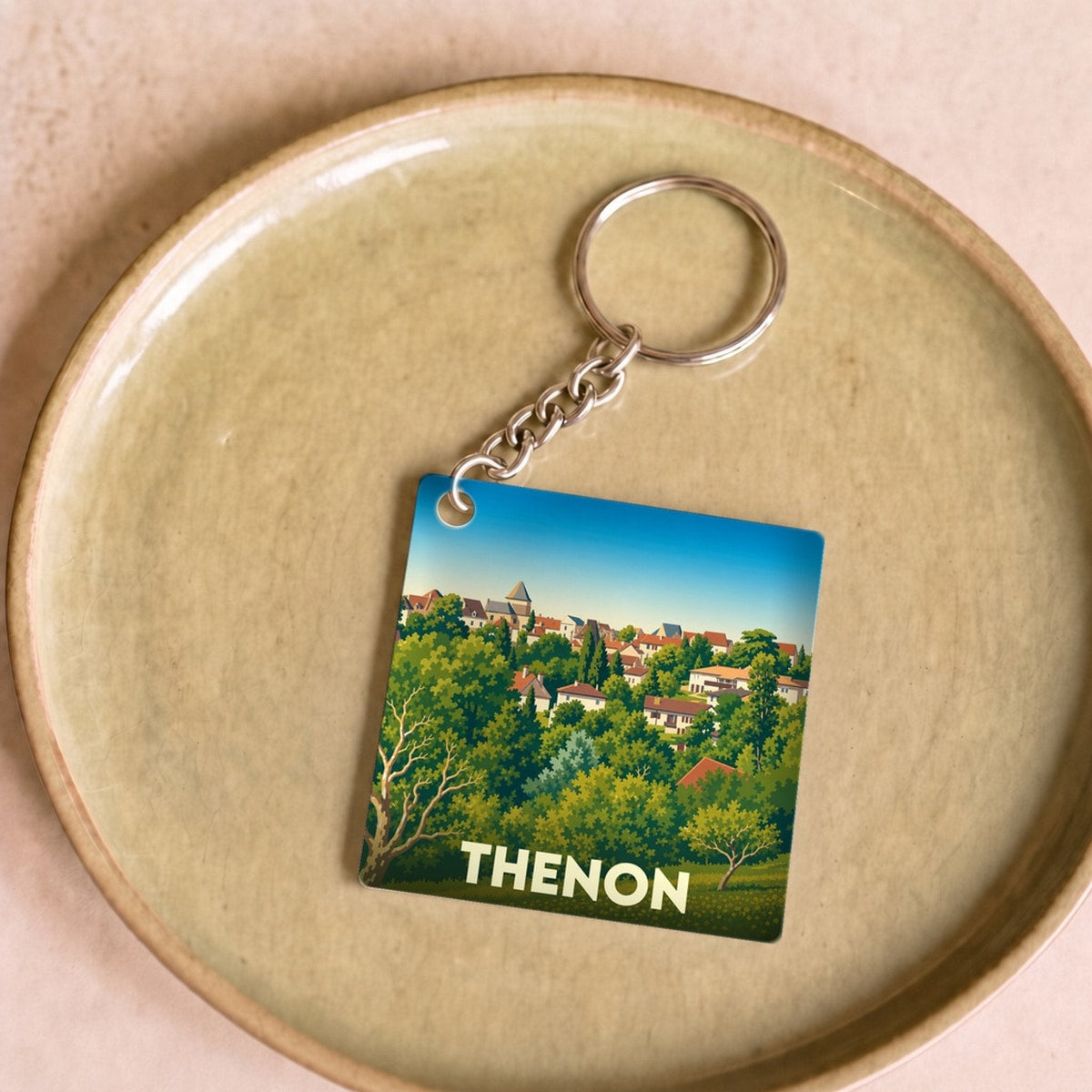 Porte-clés souvenir de la ville de Thenon avec une illustration stylisée d'un paysage urbain verdoyant.