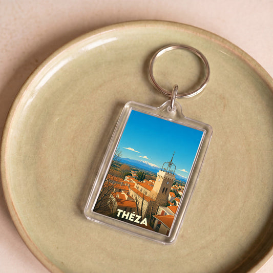 Porte-clés souvenir de la ville de Théza avec une illustration stylisée de son clocher sur fond de montagnes.