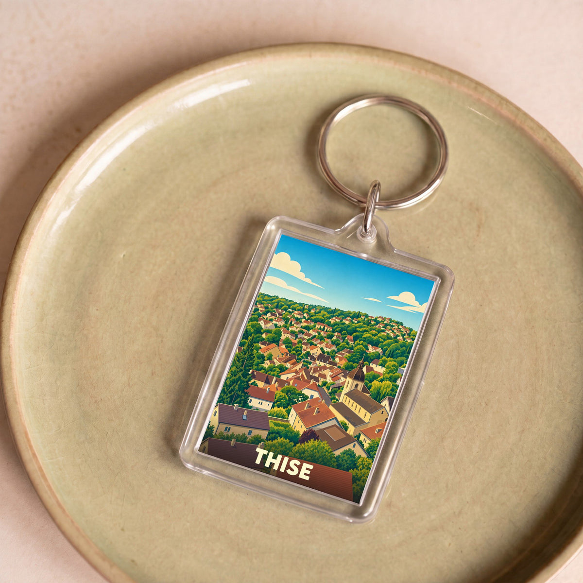 Porte-clés souvenir de la ville de Thise avec une illustration stylisée d'un paysage urbain verdoyant.