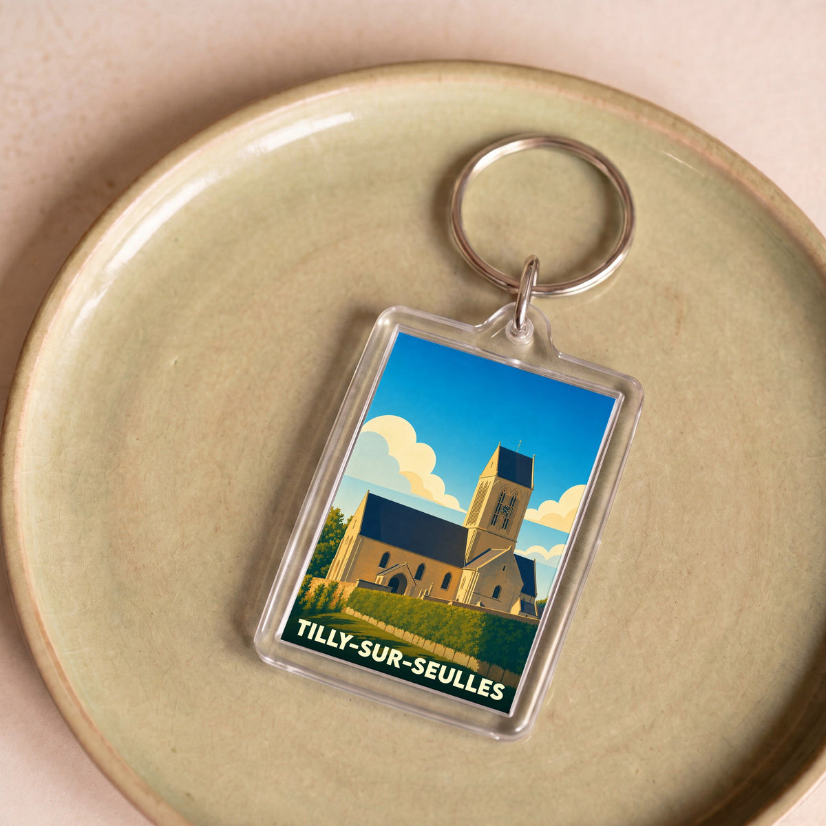 Porte-clés souvenir de la ville de Tilly-sur-Seulles avec une illustration stylisée de son église.