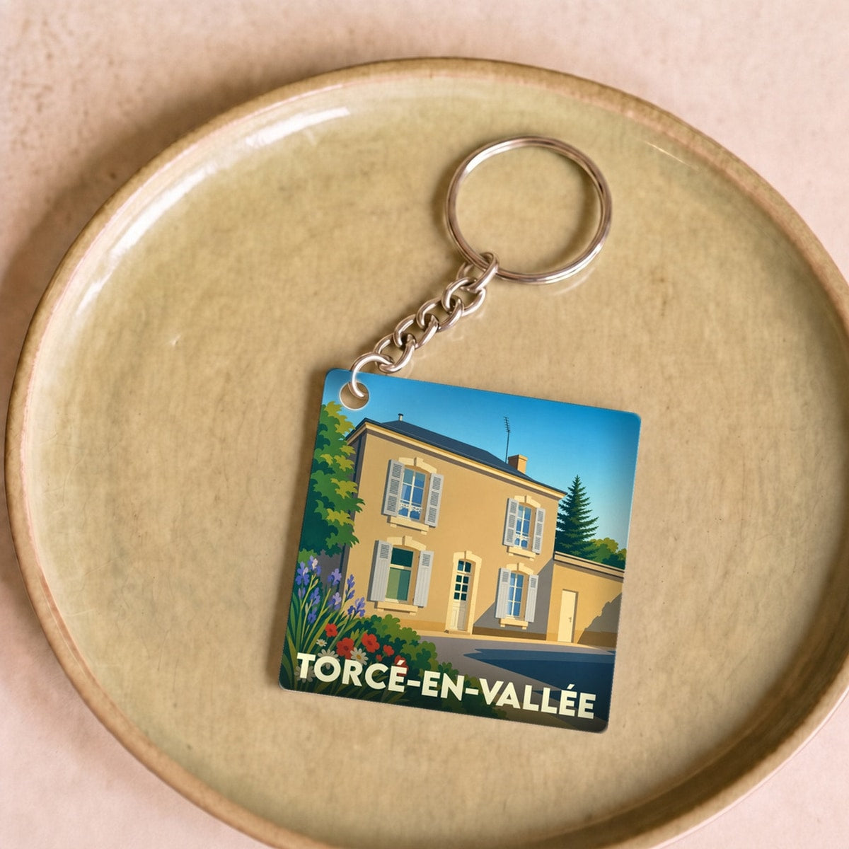 Porte-clés souvenir de la ville de Torcé-en-Vallée avec une illustration stylisée d'une maison fleurie.