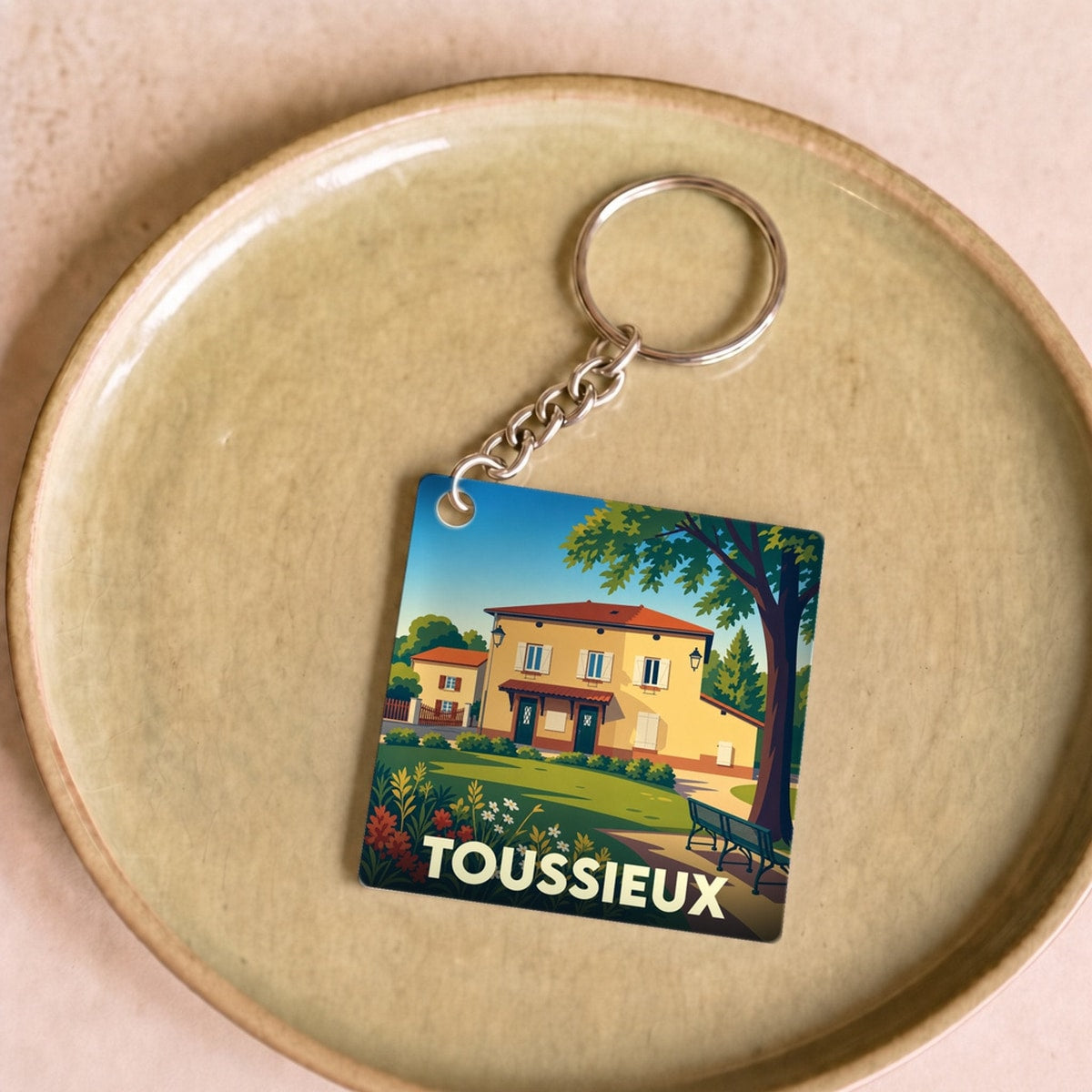 Porte-clés souvenir de la ville de Toussieux avec une illustration colorée et stylisée d'un paysage urbain.