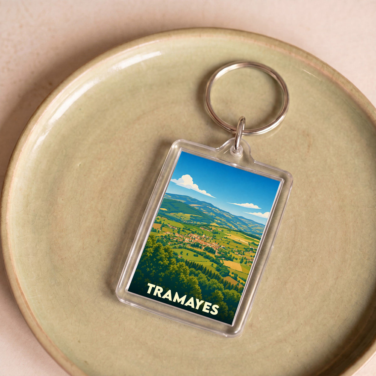 Porte-clés souvenir de la ville de Tramayes avec une illustration paysagère stylisée.