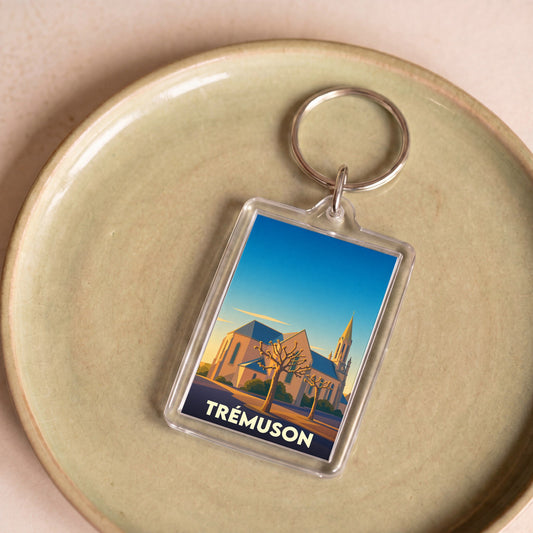 Porte-clés souvenir de la ville de Trémuson avec une illustration stylisée de son église au coucher du soleil.