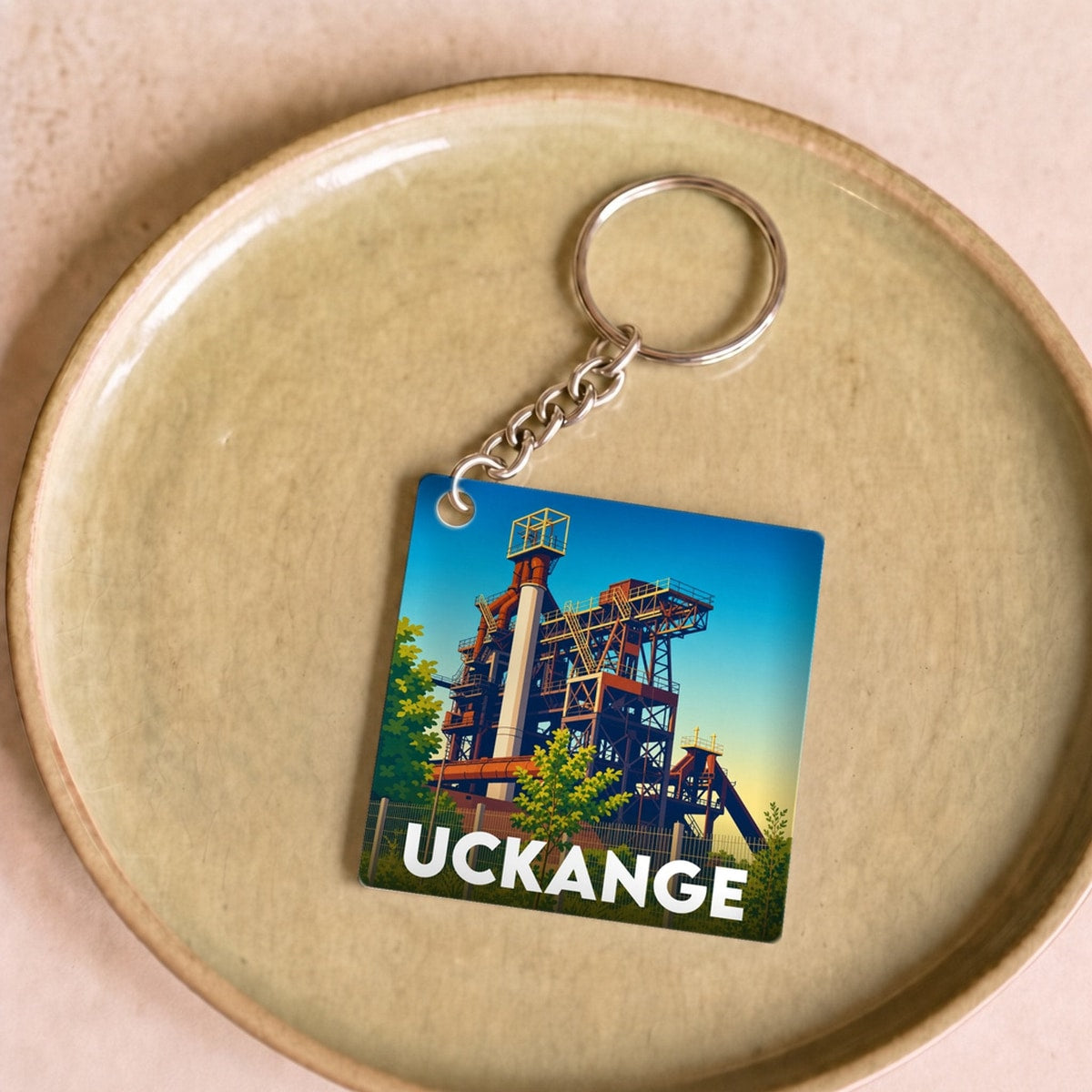 Porte-clés souvenir de la ville d'Uckange avec une illustration stylisée d'un haut-fourneau.