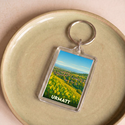 Porte-clés souvenir de la ville d'Urmatt avec une illustration stylisée de son paysage.
