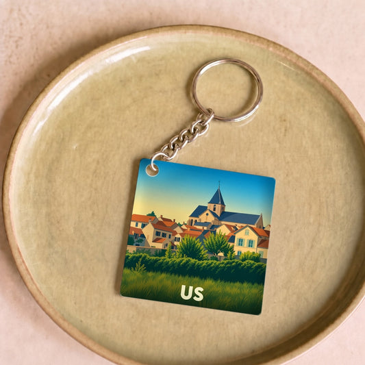 Porte-clés souvenir de la ville de Us avec une illustration stylisée d'un village pittoresque.