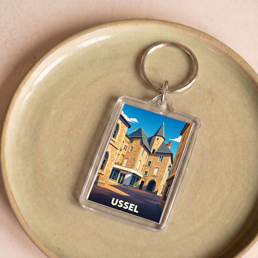 Porte-clés souvenir de la ville d'Ussel avec une illustration stylisée de son architecture historique.