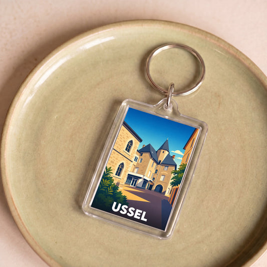 Porte-clés souvenir de la ville de Ussel avec une illustration stylisée de son architecture.